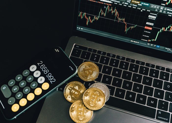 A still life of Bitcoin coins, a smartphone calculator, and a trading chart on a laptop.
